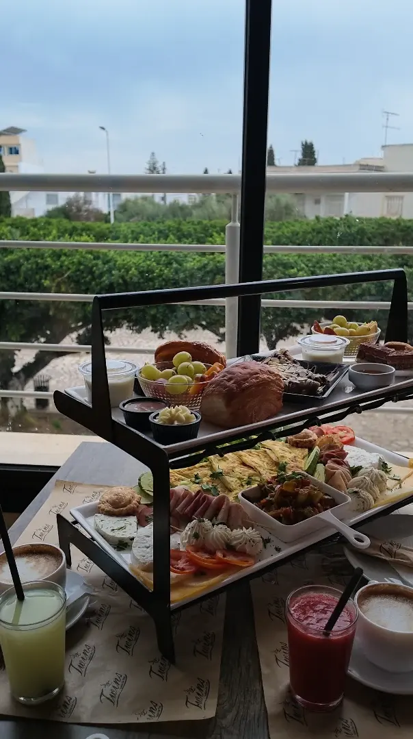 Un plateau de brunch à deux niveaux devant la baie vitrée, avec cappuccinos, jus de citron et jus rouge.