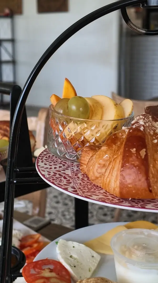 Le haut d'un présentoir à étages : croissant doré et coupe de fruits frais sur une assiette décorée.