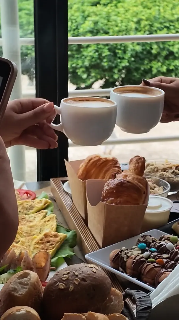 Deux tasses de cappuccino qui trinquent au-dessus des croissants et des crêpes du brunch.